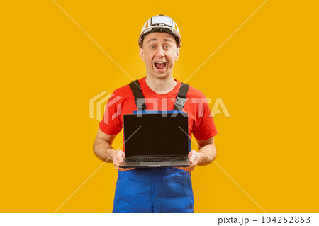 Handsome male foreman engineer holding laptop with blank screen on the yellow background. Copy space, mock up. Handsome male foreman engineer holding laptop with blank screen on the yellow background. Copy space, mock up. 104252853