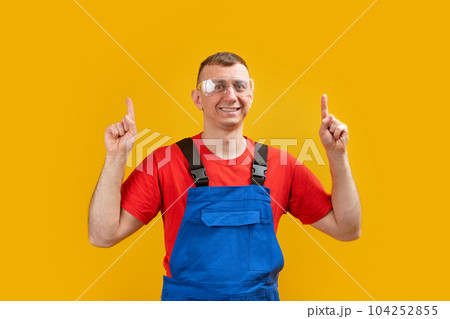 Middle-aged worker man or builder wears uniform and points his index fingers upwards. Copy space. Middle-aged worker man or builder wears uniform and points his index fingers upwards. Copy space. 104252855