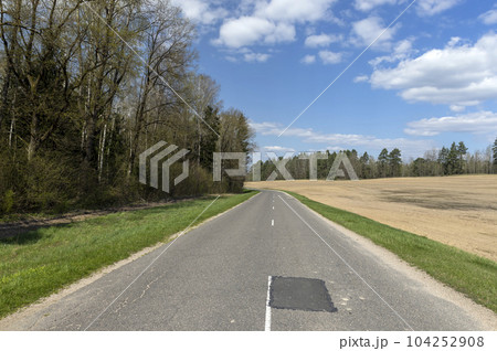 old paved road through forest and field in spring 104252908