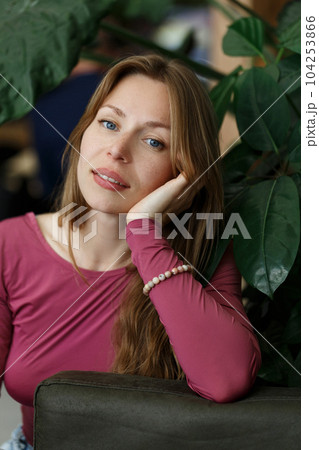 Happy young woman looking at camera. Portrait of comfortable woman relaxing on armchair. Portrait of beautiful girl smiling and relaxing on green plants background. 104253866