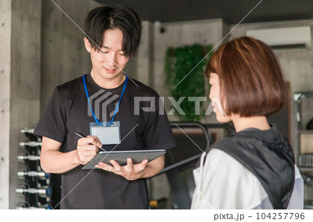 ジムでカウンセリング・運動メニューを相談するパーソナルトレーナーインストラクターの男性 104257796