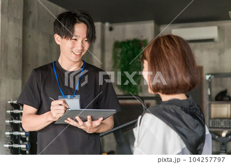 ジムでカウンセリング・運動メニューを相談するパーソナルトレーナーインストラクターの男性 104257797