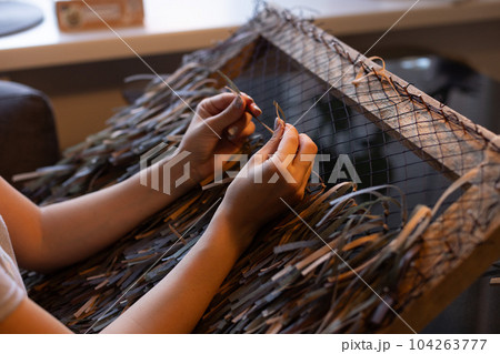 Woman weaving camouflage military mesh for helmet at home. 104263777