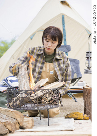 火の様子を見ながら薪を足して火を育てる若い女性　焚火　アウトドア　ソロキャンプ 104265755