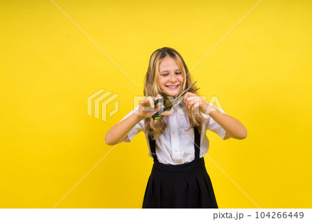 A young girl about to cut her own hair with a pair of scissors, isolated against yellow background 104266449