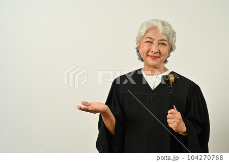 Mature female judge dressed in robe gown uniform with gavel hammer mallet isolated on white background. Law and justice concept Mature female judge dressed in robe gown uniform with gavel hammer mallet isolated on white background. Law and justice concept 104270768