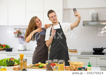 Young couple lover cooking together in the kitchen at home. Happy couple taking selfie with smartphone. Young couple lover cooking together in the kitchen at home. Happy couple taking selfie with smartphone. 104270824