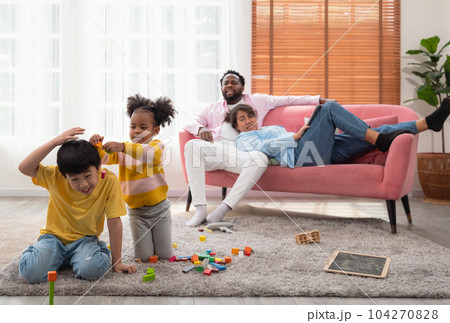 Children play with wooden toy on floor in living room while parent sitting on couch. Two kids playing with colorful blocks... 104270828