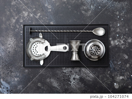 Rubber tray with stainles steel cocktail strainer,jigger and cocktail spoon on black stone Rubber tray with stainles steel cocktail strainer,jigger and cocktail spoon on black stone 104271074