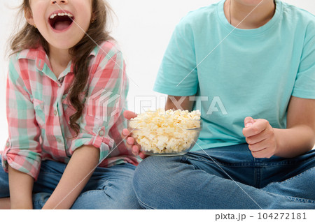 Details on a bowl of popcorn in the hands of cute cheery children watching movies or cartoons over white isolated background. People. Kids. Childhood. Lifestyle. Leisure activity. Entertainment 104272181