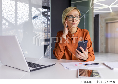 Sad upset woman pensive with phone in hands working inside office at workplace, businesswoman financier received notification message with bad news online, uses app on smartphone. Sad upset woman pensive with phone in hands working inside office at workplace, businesswoman financier received notification message with bad news online, uses app on smartphone. 104273950