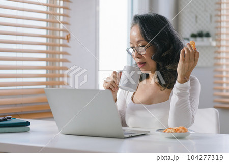Portrait of a Senior businesswoman remote working from home distance office on smartphone taking notes. Smiling 60s middle aged business lady using smartphone watching webinar and writing in notebook. Portrait of a Senior businesswoman remote working from home distance office on smartphone taking notes. Smiling 60s middle aged business lady using smartphone watching webinar and writing in notebook. 104277319