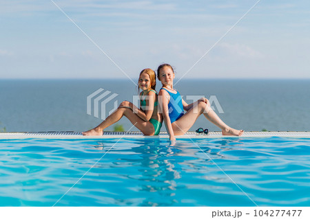 Two teenage girls sitting on the side of the pool 104277477