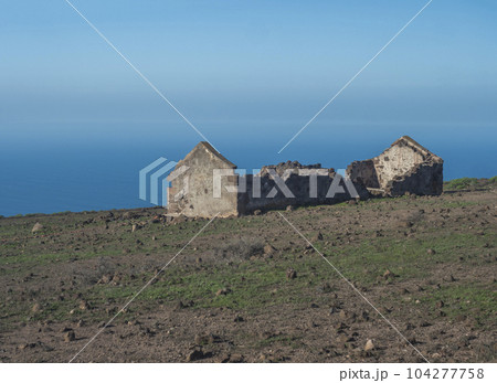 Abandoned ruins of farm house at flat plateau on top of La Merica mountain with cacti, stones and sea view. valle Gran Rey, La Gomera, Canary Islands. Copy space. Abandoned ruins of farm house at flat plateau on top of La Merica mountain with cacti, stones and sea view. valle Gran Rey, La Gomera, Canary Islands. Copy space. 104277758