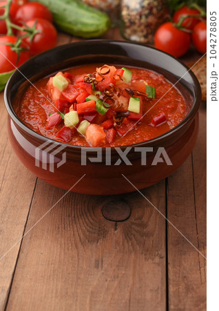 Cold summer gazpacho soup in bowl with ingredients on wood board desk. Copy space on brown wooden background. Recipe of tomato summer soup. Tomato, pepper, garlic, cucumber, greens. Menu. Cold summer gazpacho soup in bowl with ingredients on wood board desk. Copy space on brown wooden background. Recipe of tomato summer soup. Tomato, pepper, garlic, cucumber, greens. Menu. 104278805