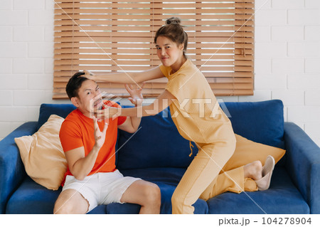 Funny husband and wife fighting on the sofa in the house. 104278904