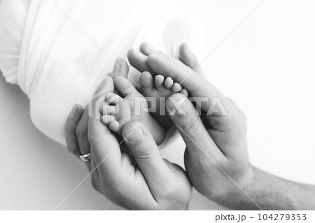 The palms of the father, the mother are holding the foot of the newborn baby on white background. Feet of the newborn on the palms of the parents. Photography of a child's toes, heels and feet. The palms of the father, the mother are holding the foot of the newborn baby on white background. Feet of the newborn on the palms of the parents. Photography of a child's toes, heels and feet. 104279353