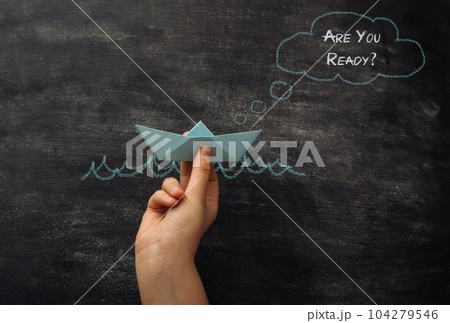 hand holds paper boat against the background of board with text Are You Ready 104279546