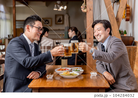 居酒屋で同僚・友達と飲み会・ビールで乾杯をするスーツ姿のビジネスマン・サラリーマンの男性 104284032