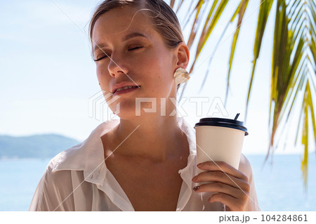 Woman hold takeaway coffee cup walking by seashore. Summery female portrait. 104284861