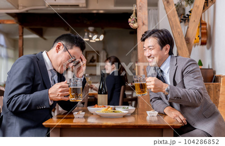 居酒屋で酒・ビールを飲みながら同僚・友達と楽しく会話するビジネスマン 104286852