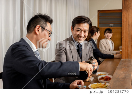 飲み屋のカウンターで上司や同僚にお酌する笑顔のビジネスマン 104288770