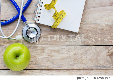 Top view green apple with blue stethoscope and notebook on wood table background Top view green apple with blue stethoscope and notebook on wood table background 104290497