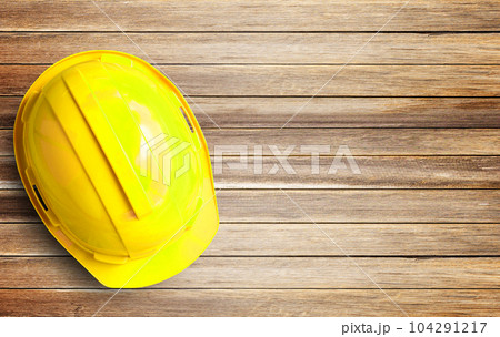Yellow safety helmet and white paper on Brown old wood background Yellow safety helmet and white paper on Brown old wood background 104291217