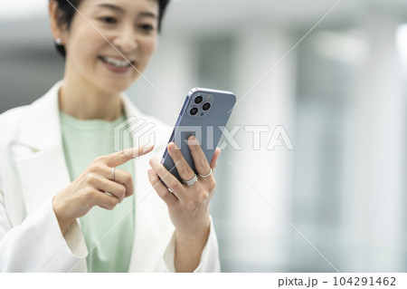 スマートフォンを操作するアラフィフのビジネスウーマンの手元 104291462