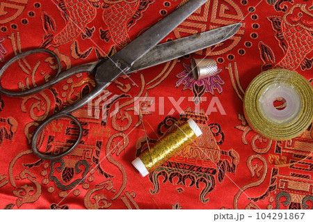 Spool of Gold Metallic Thread and Thimble on Vintage Red Silk Fabric Spool of Gold Metallic Thread and Thimble on Vintage Red Silk Fabric 104291867