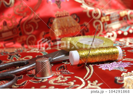 Spool of Gold Metallic Thread and Thimble on Vintage Red Silk Fabric Spool of Gold Metallic Thread and Thimble on Vintage Red Silk Fabric 104291868