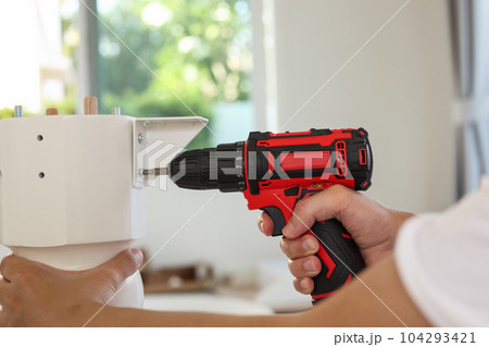 man assembling white table furniture at home using cordless screwdriver 104293421