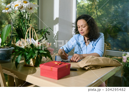 Portrait of female florist entrepreneur freelancer writing notes on clipboard, drawing composition of flowers for special events, sitting at table in her home flower shop. Business. Creativity. People Portrait of female florist entrepreneur freelancer writing notes on clipboard, drawing composition of flowers for special events, sitting at table in her home flower shop. Business. Creativity. People 104295482