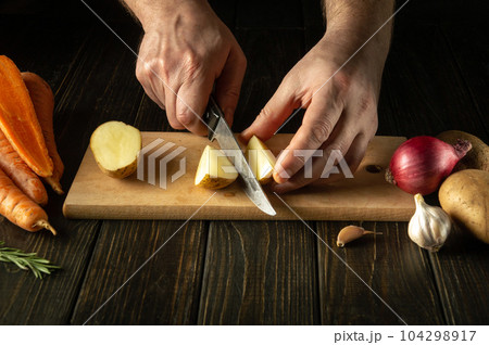 The cook cuts the potatoes in the kitchen with a knife to prepare a national dish or mashed potatoes. Delicious vegetable diet. 104298917