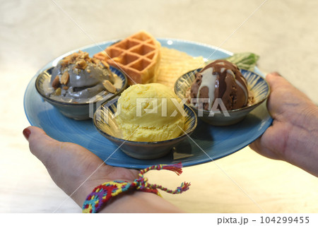 Woman's hand holding homemade ice cream with waffle on plate with chocolate syrup Woman's hand holding homemade ice cream with waffle on plate with chocolate syrup 104299455