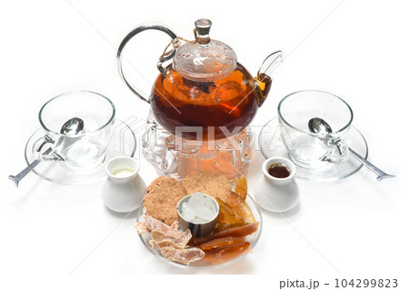 Earl Grey tea in glass teapot with cups and crystalized fruits on white background Earl Grey tea in glass teapot with cups and crystalized fruits on white background 104299823
