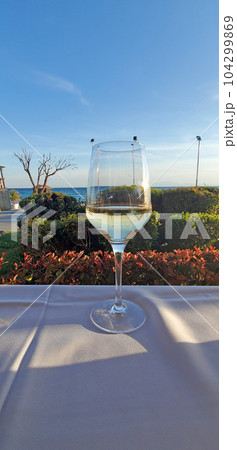 A glass of white wine on a table with a white tablecloth in an open-air cafe 104299869
