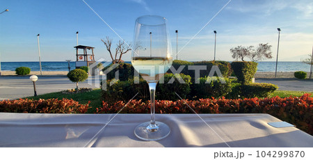A glass of white wine on a table with a white tablecloth in an open-air cafe A glass of white wine on a table with a white tablecloth in an open-air cafe 104299870