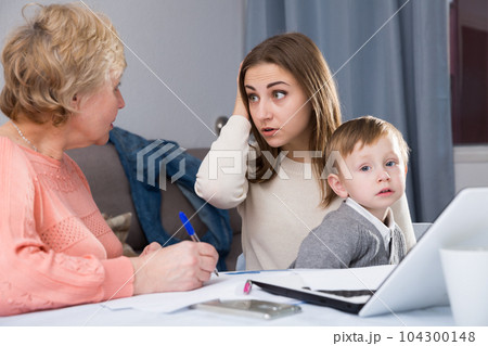 Puzzled aged woman is mastering technology near laptop with her daughter and grandson 104300148
