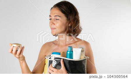 A woman after a shower with a cosmetic bag in her hands - chooses a cream, self-care at home A woman after a shower with a cosmetic bag in her hands - chooses a cream, self-care at home 104300564