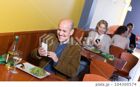 Mature man with mobile at the table in cafe. Mature man with mobile at the table in cafe. 104300574