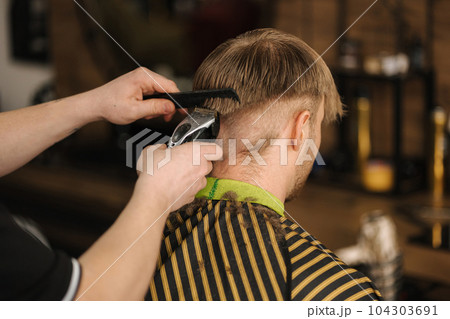 Back view of barber using trimmer to make haircut for customer Back view of barber using trimmer to make haircut for customer 104303691