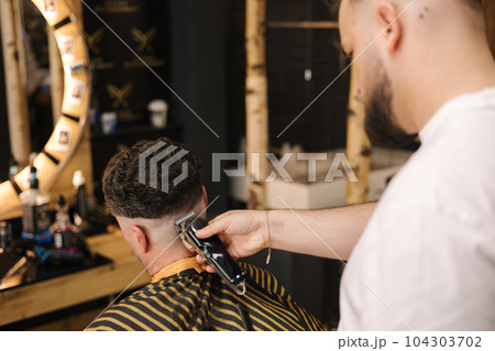 Man sitting in barber shop during barber have cut his hair. Back view of process Man sitting in barber shop during barber have cut his hair. Back view of process 104303702