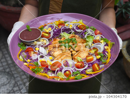 Hands holding dish with pan fried chicken and vegetables Hands holding dish with pan fried chicken and vegetables 104304170