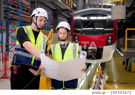 Young caucasian engineer man and woman or worker looking blueprint and checking electric train. 104305672