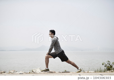 young asian adult man stretching legs outdoors by the sea young asian adult man stretching legs outdoors by the sea 104306303