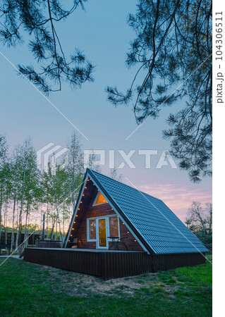 A-frame wooden cabin with light inside in evening 104306511