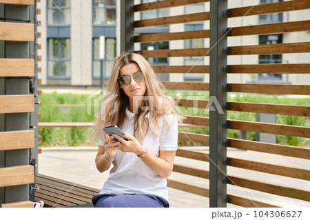 Woman in sunglasses on bench with smartphone Woman in sunglasses on bench with smartphone 104306627