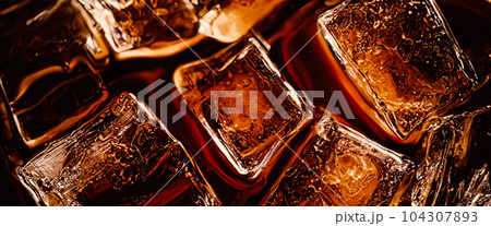 Cola with Ice. Close up of the ice cubes in cola water. Texture of carbonate drink with bubbles in glass. Cola soda and ice splashing fizzing or floating up to top of surface. Cold drink background. Cola with Ice. Close up of the ice cubes in cola water. Texture of carbonate drink with bubbles in glass. Cola soda and ice splashing fizzing or floating up to top of surface. Cold drink background. 104307893