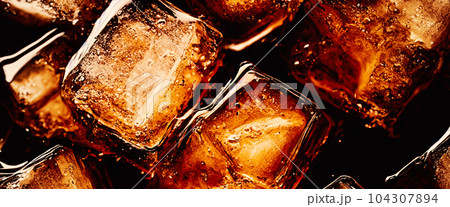 Cola with Ice. Close up of the ice cubes in cola water. Texture of carbonate drink with bubbles in glass. Cola soda and ice splashing fizzing or floating up to top of surface. Cold drink background. Cola with Ice. Close up of the ice cubes in cola water. Texture of carbonate drink with bubbles in glass. Cola soda and ice splashing fizzing or floating up to top of surface. Cold drink background. 104307894